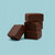 A stack of three thick squares of smooth, dark chocolate fudge, with a fourth square leaning against the base, is displayed against a solid light blue background.