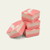 A stack of three square pieces of pink and white swirled raspberry vanilla fudge, with a fourth piece leaning against the base, set against a solid off-white background.