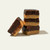 A stack of three square pieces of two-layered chocolate and peanut butter fudge, with a fourth piece leaning against the base, set against a solid off-white background.