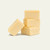 A stack of three square pieces of vanilla fudge, with a fourth piece leaning against the base, set against a solid off-white background.