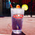 Purple drink in a Fudge Packers Union pint glass on an outdoor table with a fence background at Uranus Fudge Factory.