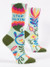 A pair of light mint green crew socks displayed against a plain white background. The socks feature olive green accents on the toe, heel, and top edge. They are decorated with a vibrant, bold floral pattern featuring stylized vines, leaves, and large flowers in bright pink, orange, blue, and yellow. Knit into the upper ankle of the front sock, sandwiched between two large colorful floral shapes, is the blue block text: "STOP TALKING".