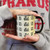 Person holding a cream Route 66 coffee mug with a black handle from Uranus Fudge Factory.