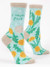 A pair of light aqua blue crew socks displayed against a plain white background. The socks feature tan accents on the toe, heel, and top cuff. They are decorated with a nature pattern of yellow dandelion flowers, jagged green leaves, and a white dandelion seed head with tiny seeds blowing away in the wind.