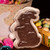 Chocolate Easter bunny shaped fudge from Uranus Fudge Factory in clear packaging, surrounded by colorful Easter eggs and a festive basket.