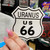 A hand holding a white Uranus US 66 highway shield shape novelty magnet from Uranus Fudge Factory