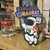 Cartoon astronaut sticker with Uranus Branding displayed on a wooden shelf next to souvenir shot glasses at Uranus Fudge Factory.