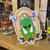 Rainbow alien peace sign with Uranus branding sticker displayed on a wooden shelf next to souvenir shot glasses at Uranus Fudge Factory.