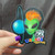 Green alien punk with planet sticker held by a hand with purple nail polish against a dark cloth backdrop by Uranus Fudge Factory.