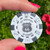 Route 66 souvenir poker chip held up close against a vibrant green outdoor foliage background by Uranus Fudge Factory.