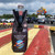 Zippered bottle koozie holding a soda bottle on a picnic table with a parking lot behind by Uranus Fudge Factory.