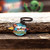 Rocket and planet logo keychain resting on wood next to a key from Uranus Fudge Factory.
