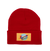 A bright red knit cuffed beanie hat against a plain white background. The front cuff features a sewn-on rectangular yellow patch. The patch displays a light blue planet with a retro red and white rocket ship flying across it, leaving a trail of orange flames.