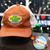Burnt orange Gas N Lube trucker hat displayed with green alien figure and sticker at Uranus Fudge Factory.