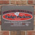 Uranus Fudge Packer's Union 12x16 metal sign mounted on a red brick wall, featuring the red and white Fudge Packers Union oval logo, Local #2 chef's hat, and "Proudly Packing Fudge In Uranus Since 2015" tagline.