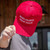 Hand holding up the red Make Uranus Great Again hat, white embroidered lettering facing forward.