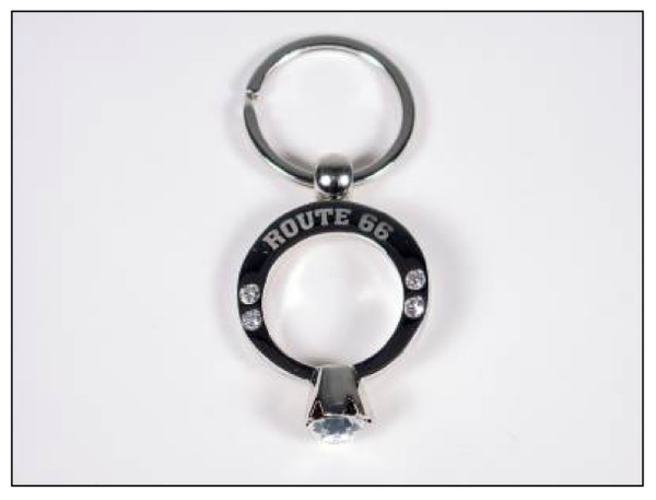 A silver metal souvenir keychain shaped like a diamond engagement ring with Route 66 text and rhinestones