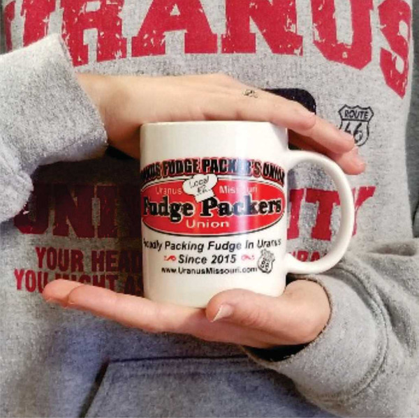 Fudge Packers Union Local #2 15oz coffee mug held by a person from Uranus Fudge Factory