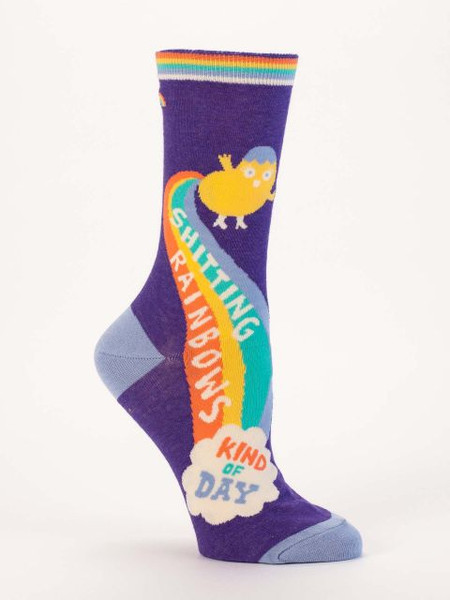 A single dark purple crew sock displayed against a plain white background. The sock features light blue accents on the toe and heel, and a rainbow-striped top cuff. Knit into the side is a small, round yellow cartoon character shooting a colorful rainbow from its backside down into a fluffy white cloud.