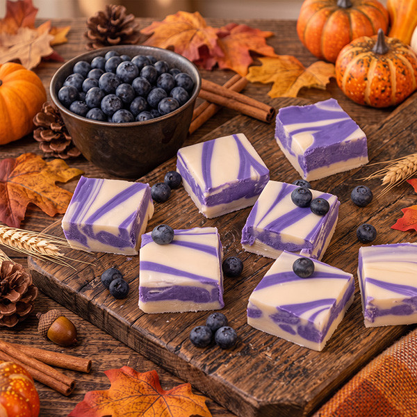 Purple and vanilla blueberry swirl fudge squares with a bowl of blueberries and autumn decor on a rustic table