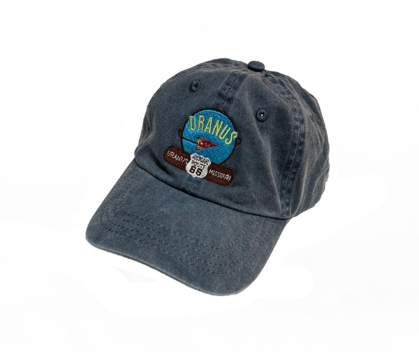 Faded blue baseball cap featuring an embroidered Uranus Missouri space rocket patch on a white background Uranus Fudge Factory.