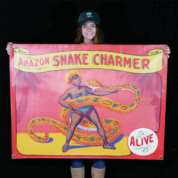 A person holding up a vintage-style Amazon Snake Charmer carnival sideshow banner from Uranus Fudge Factory