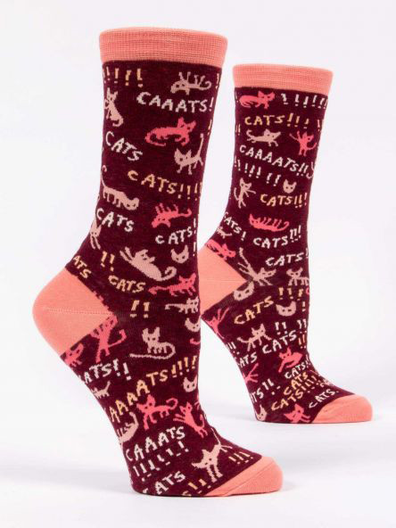 A pair of dark burgundy crew socks displayed against a plain white background. The socks feature peach-colored accents on the toe, heel, and top cuff. They are covered in a chaotic, all-over pattern of stylized pink and peach cat silhouettes in various poses, mixed with the words "CATS!!!" and "CAAATS!!!" repeated wildly with multiple exclamation points.