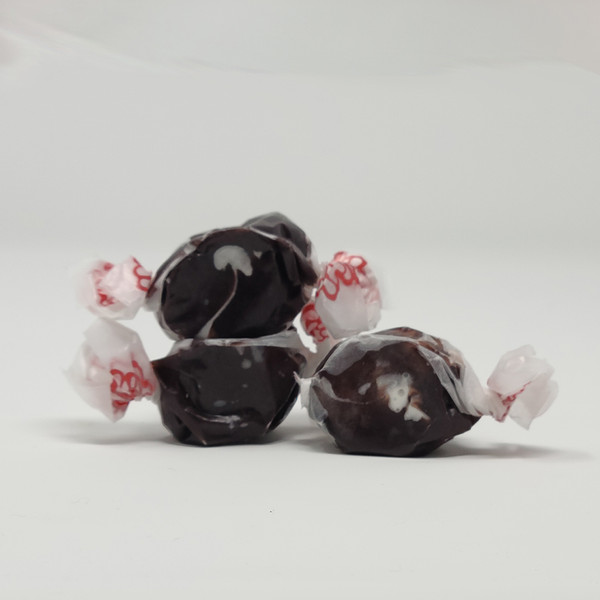 Three pieces of black salt water taffy candies with white details wrapped in wax paper.