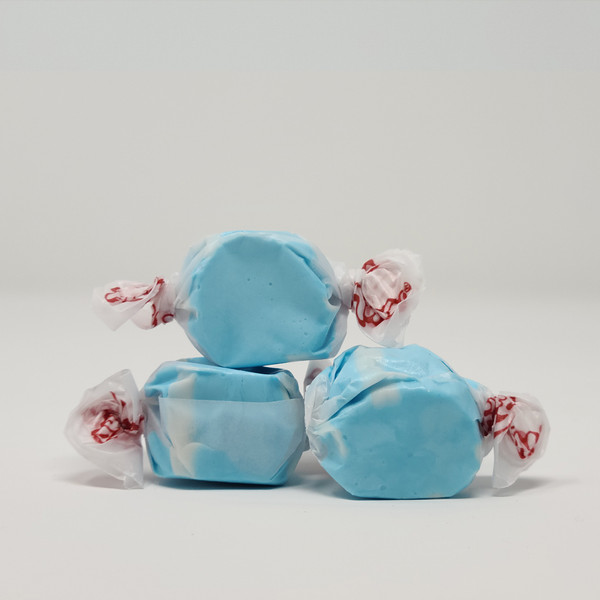 Three pieces of blue salt water taffy candies with white details wrapped in wax paper.
