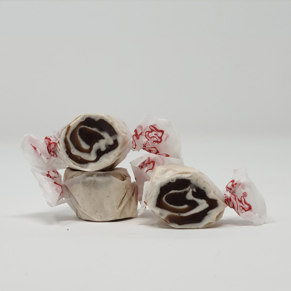 Three pieces of white salt water taffy candies with brown swirls wrapped in wax paper.