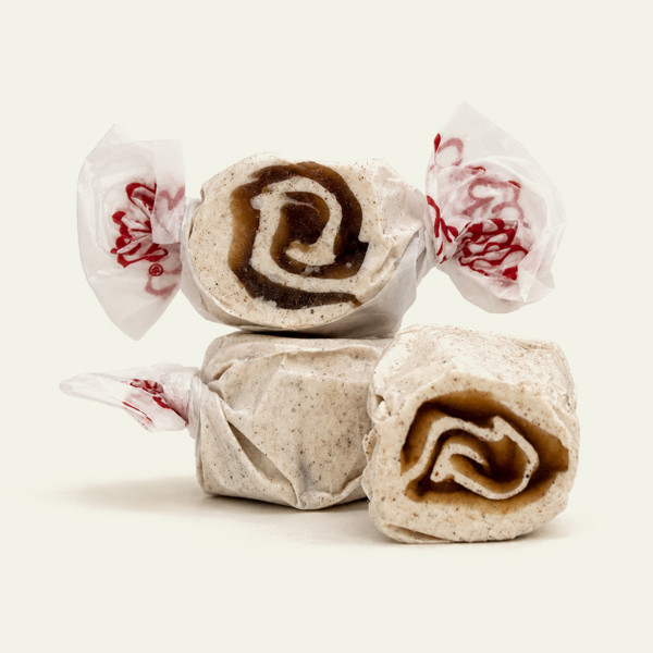 Three pieces of white salt water taffy candies with brown swirls wrapped in wax paper.
