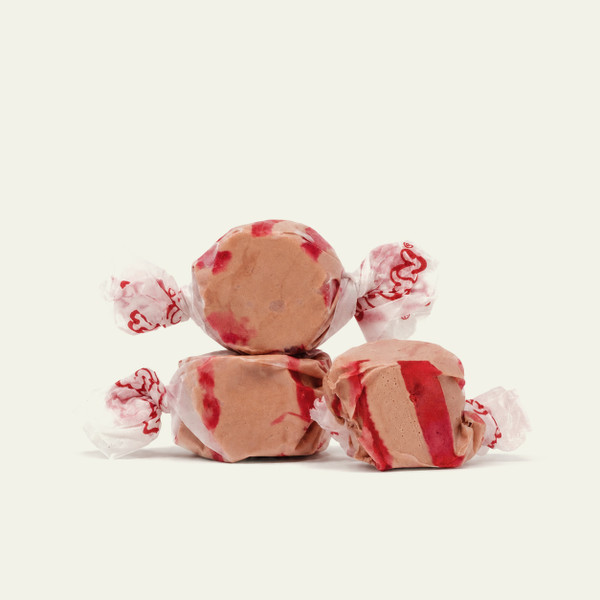 Three pieces of tan salt water taffy candies with red stripes wrapped in wax paper.
