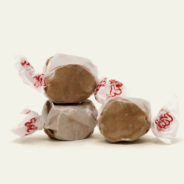 Three pieces of light brown salt water taffy candies wrapped in wax paper.