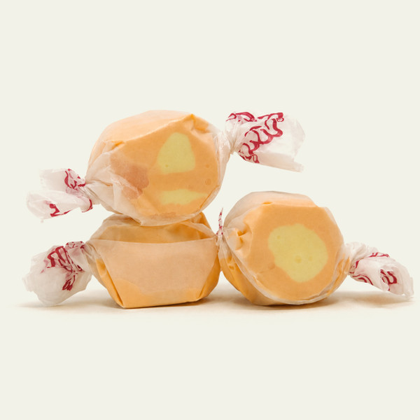 Three pieces of orange salt water taffy candies with yellow center wrapped in wax paper.