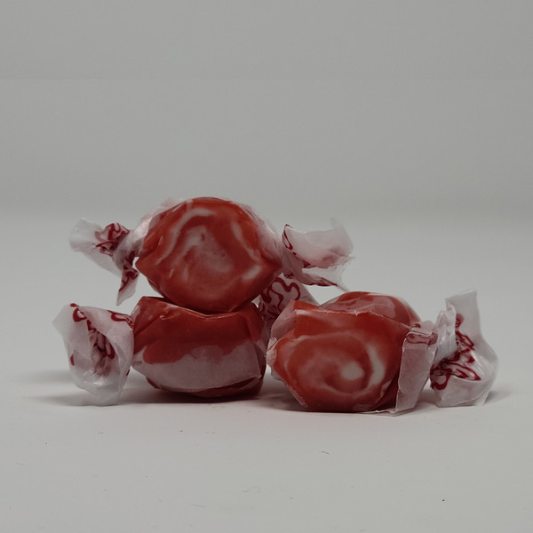  Three pieces of red salt water taffy candies with white swirls wrapped in wax paper.