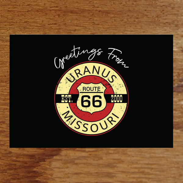 A horizontal postcard featuring a solid black background with white cursive text reading "Greetings From" centered at the top. Below is a distressed, circular vintage-style emblem with a Route 66 shield in the red center, framed by a yellow ring reading "URANUS MISSOURI" and crossed by a black banner reading "EST. 2000".