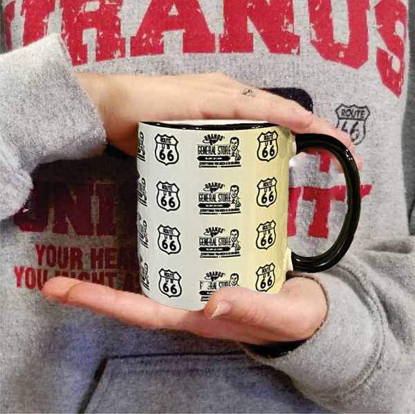 Person holding a cream Route 66 coffee mug with a black handle from Uranus Fudge Factory.