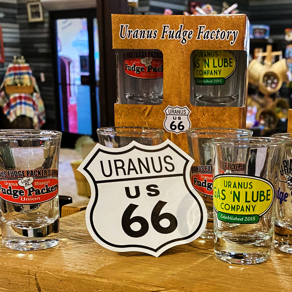 White Uranus US 66 shield sticker displayed with novelty shot glasses from Uranus Fudge Factory