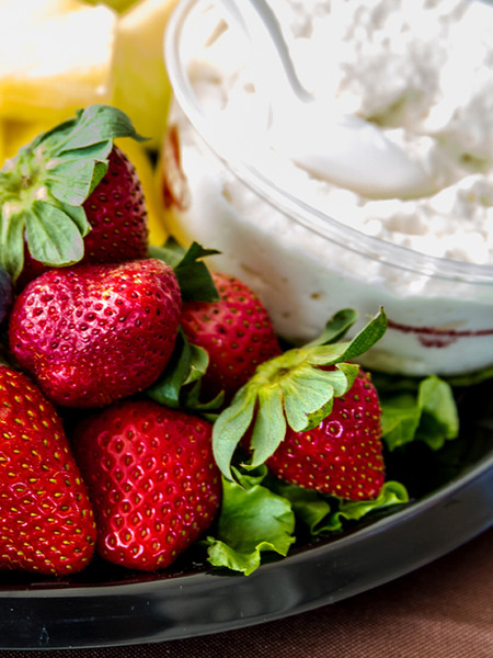 Fresh red strawberries arranged on a plate next to a bowl of creamy white dip by Uranus Farms.