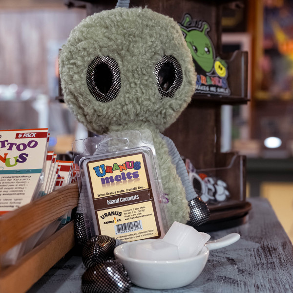 Island Coconuts wax melts pack leaning against an alien plush doll from Uranus Fudge Factory.