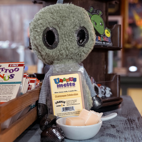 Champagne Celebration wax melts pack leaning against an alien plush doll from Uranus Fudge Factory.