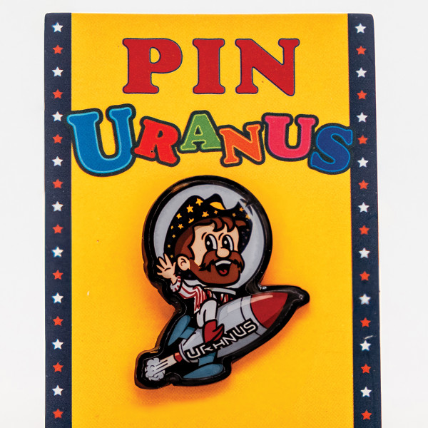 Rex Uranus riding a rocket hat pin attached to a yellow Pin Uranus card from Uranus Fudge Factory.