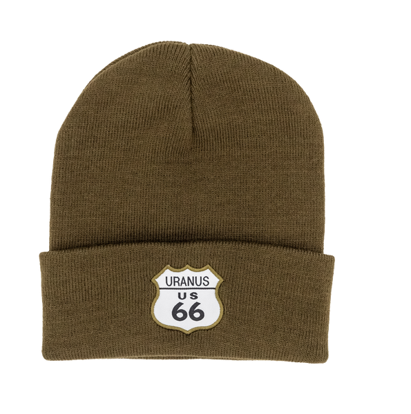 A dark olive green knit cuffed beanie hat against a plain white background. The front cuff features a sewn-on white patch shaped like a classic highway shield with an olive green border.