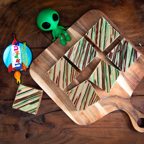 Irish Cream Fudge squares on a wooden cutting board. A green alien sits on the edge of the board. The Uranus logo is visible. 
