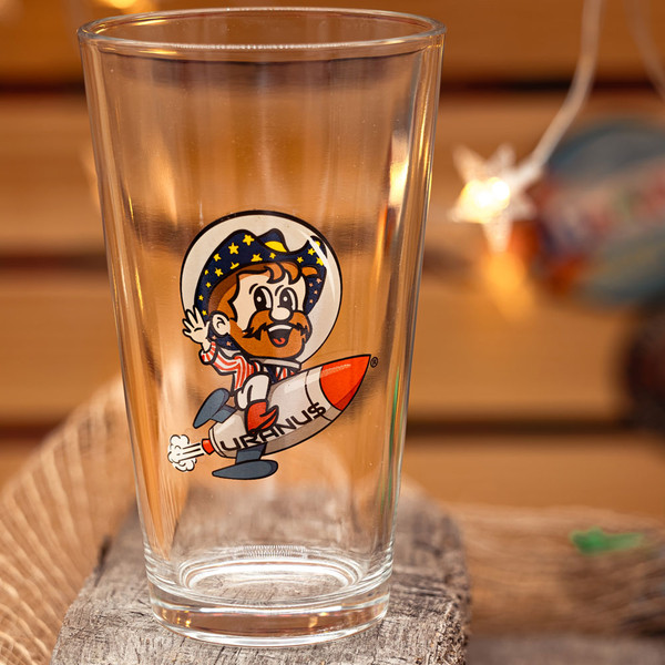 Clear pint glass with Rex Uranus rocket graphic displayed on wood from Uranus Fudge Factory.