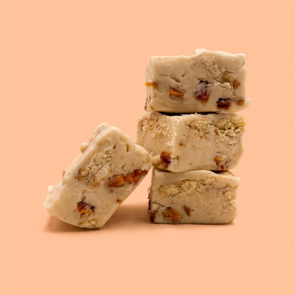 A pound of Peach Cobbler Fudge in a stack of 3 with a fourth square leaning against it. The background is peach. 