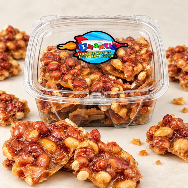 Uranus Fudge Factory peanut brittle in a clear 1 lb. tub with broken pieces of glossy peanut brittle in the foreground