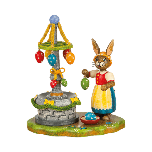 Mrs. Rabbit is decorating the village fountain with colorful ribbons and eggs for Easter.