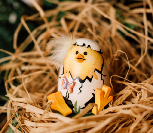 Easter themed pyramid with flower tealight candle holders and three rabbits on a small table with a coffee pot, cup and plate with pastry and a vase with daffodils. 
