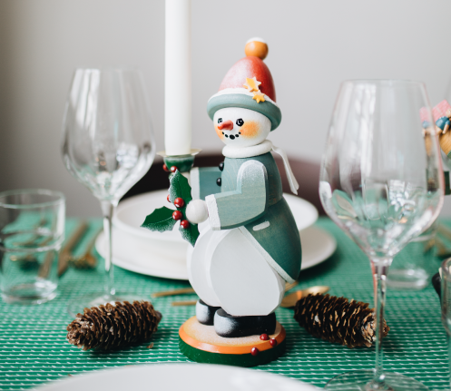 Easter themed pyramid with flower tealight candle holders and three rabbits on a small table with a coffee pot, cup and plate with pastry and a vase with daffodils. 